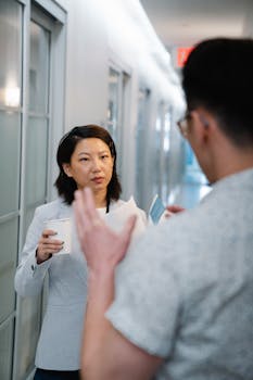 A man and woman having a conversation in a modern office hallway.