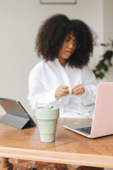 Woman working from home using laptop and tablet, enjoying a coffee break.